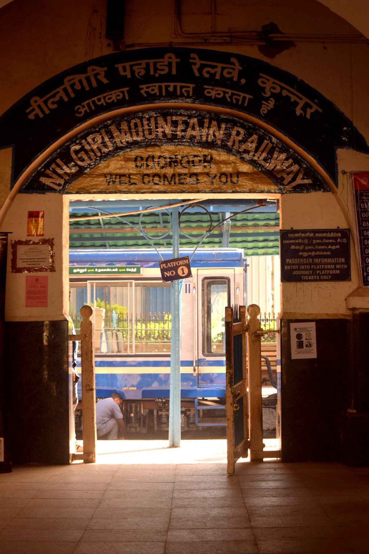 The Nilgiri Mountain Railway heritage archway framing the blue toy train at Coonoor station